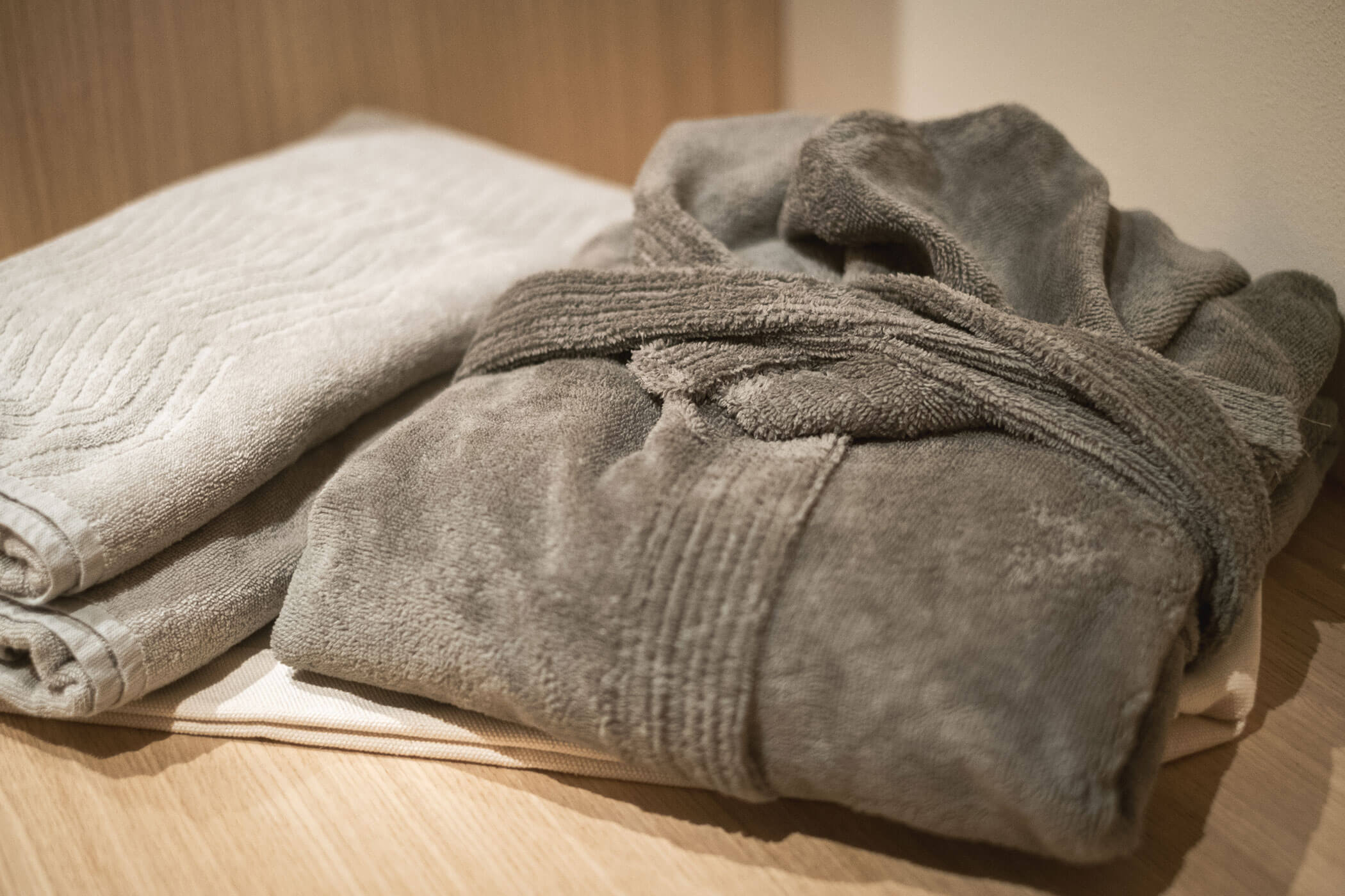 Dark bathrobe with light grey towels next to it - Gisse Zwölf