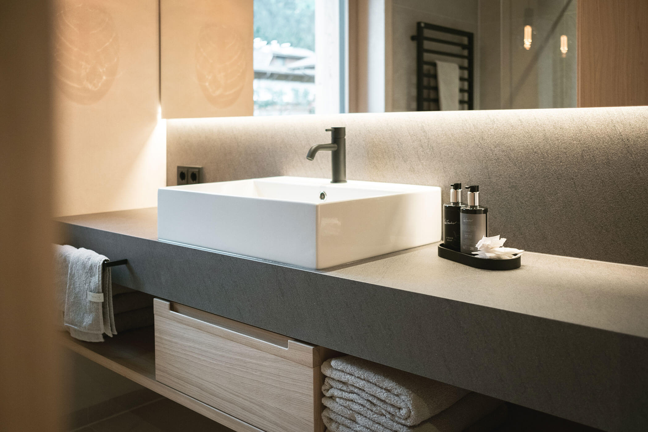 White washbasin, two soap dispensers next to it and light-colored towels underneath - Gisse Zwölf
