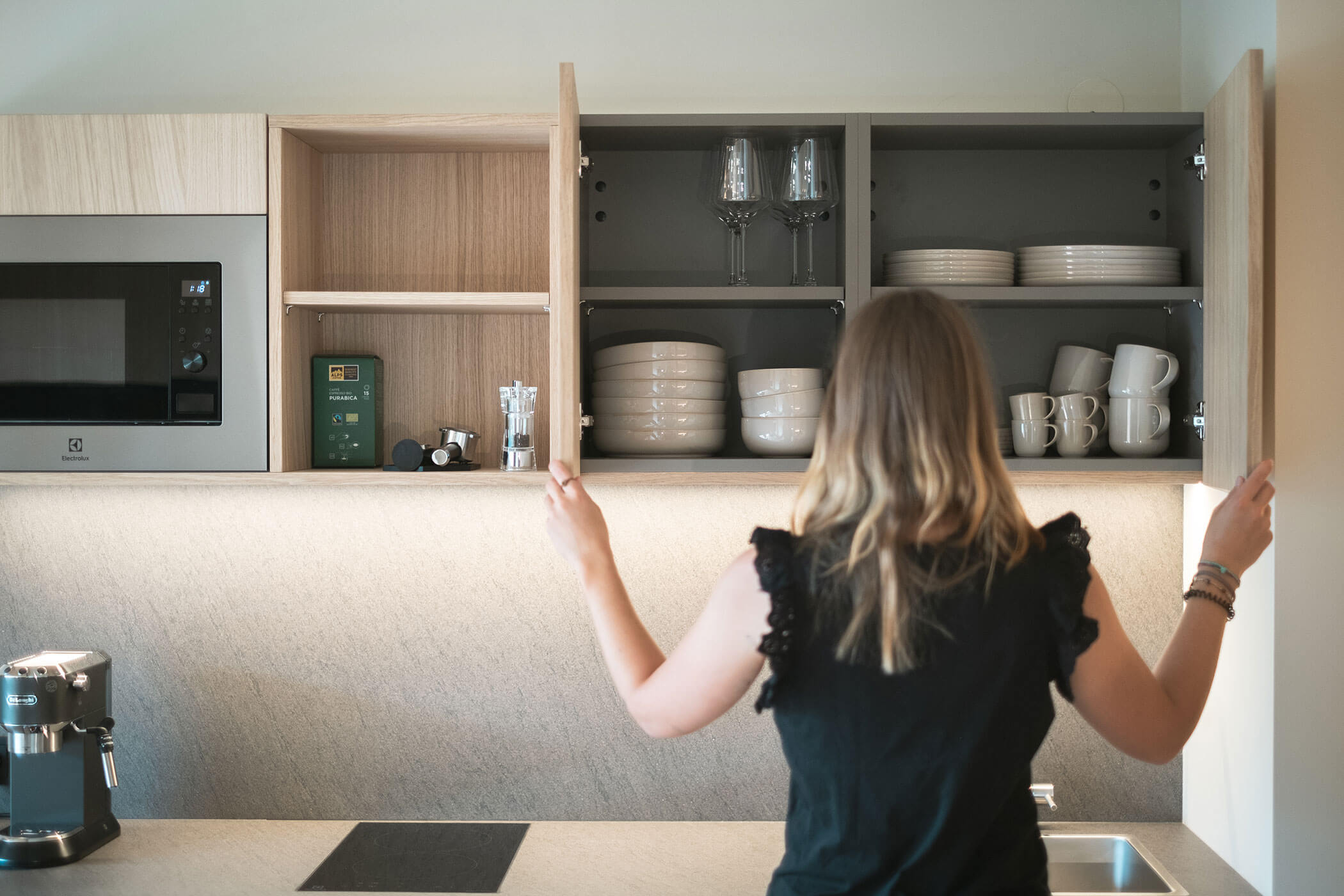 Woman opens the cupboard door, inside cups, plates and wine glasses - Gisse Zwölf